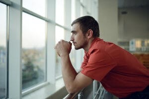 Man in red shirt looking out window worrying about his heroin addiction