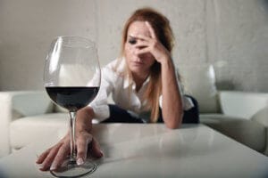 Sad woman at table looking at wine knowing she needs alcohol treatment